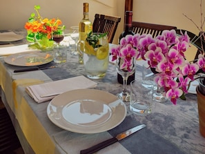 Een eettafel gedekt met borden, bestek, een fles wijn, een kan met citroenen en orchideeën.