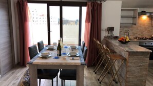 Een eethoek met een tafel voor vier personen, een keuken met een gasfornuis en uitzicht door het raam.