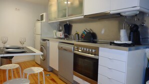 A compact kitchen with a washing machine, dishwasher, oven, and a microwave. There are stools at a small table and a sink with a kettle. - Best in Alfama - Free pick up (Lisboa - Alfama)