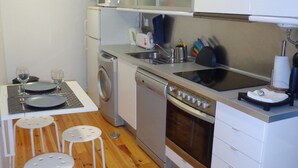 A compact kitchen with a washing machine, a microwave, a stove, and a sink. There are white cabinets and a wooden floor. - Best in Alfama - Free pick up (Lisboa - Alfama)
