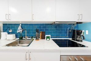 Une cuisine moderne avec des meubles blancs, un pare-feu bleu, une cuisinière noire et une machine à café.