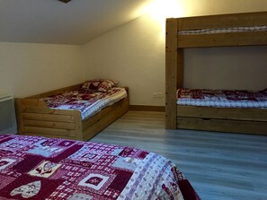 A room with two wooden bunk beds, one with a quilt and one with a plain sheet.