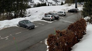 Ein Parkplatz mit Autos und einer Seilbahn im Hintergrund.