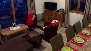 Ein Wohnzimmer mit Fernseher, einem Esstisch für vier Personen und einem Balkon mit Blick.