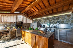 Une cuisine rustique avec un mur en pierre, des poutres en bois et un grand îlot central doté d’un évier et d’une cuisinière.