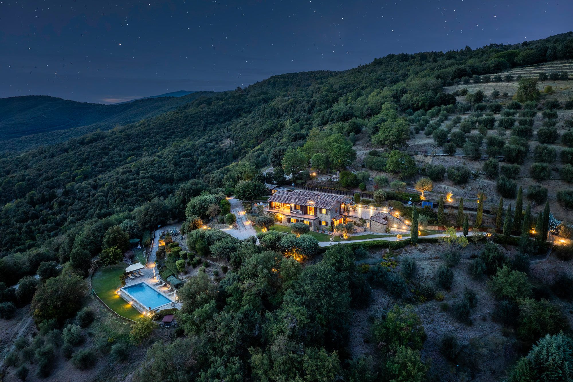 A large estate with a swimming pool, multiple outdoor lighting, and a surrounding landscape.