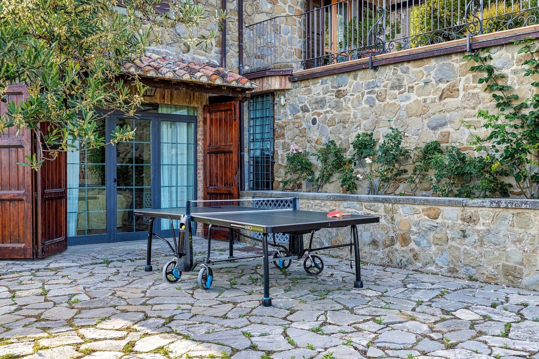 Une cour avec une table de ping-pong, des murs en pierre et une porte en bois.