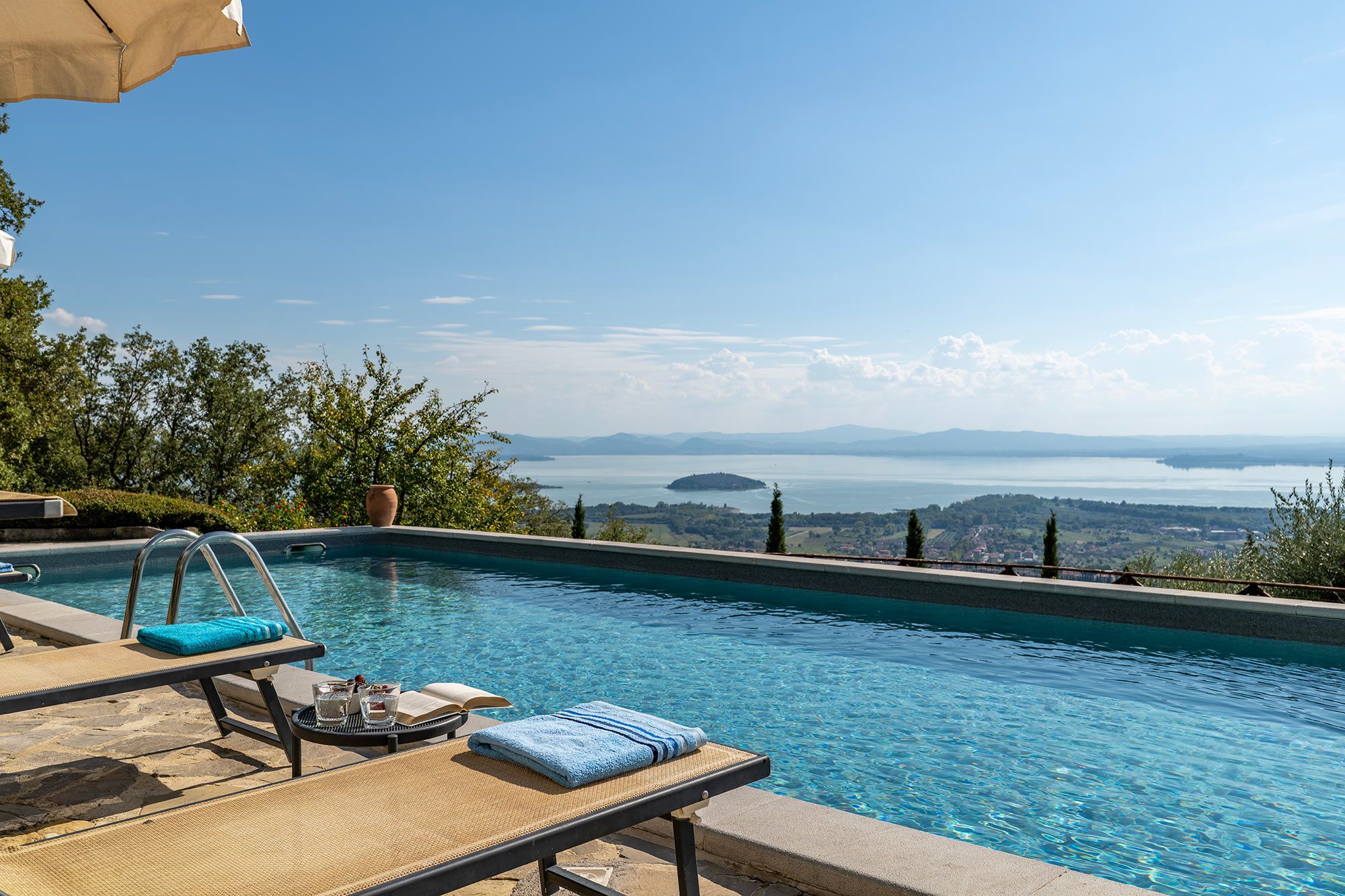Une piscine dotée de chaises longues, offrant une vue sur un lac et des montagnes lointaines.