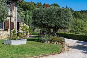 Un bâtiment en pierre doté d’un balcon, entouré de jardins bien entretenus et bordé d’un chemin de gravier.