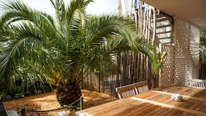Ein Holztisch mit Stühlen, eine Zierpflanze und ein Gitterzaun in einem Garten.