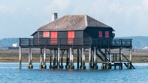 A wooden house with red shutters on a pier over water.