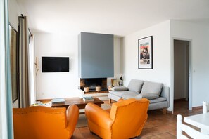 A living room with a sofa, armchairs, a coffee table, a flat-screen TV, and a fireplace.
