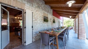 A dining area with a long wooden table, stone walls, and a view of the outdoors. - Cascina Marianna 12+4, Emma Villas (Fossombrone)