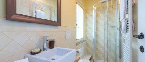 A bathroom with a sink, mirror, towel rack, shower, and toilet.