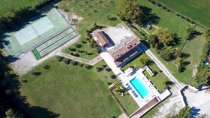 An aerial view of a property with a tennis court, a swimming pool, and a building with a tiled roof. - Cascina Marianna 12+4, Emma Villas (Fossombrone)