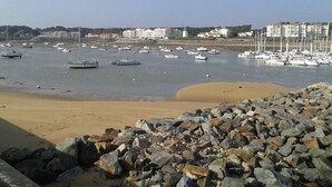 Un paysage côtier avec une plage rocheuse, une marina où sont amarrés de nombreux bateaux et des bâtiments en arrière-plan.
