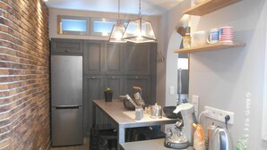 A modern kitchen with a brick wall, grey cabinets, a stainless steel refrigerator, a hanging light fixture, and a coffee maker.