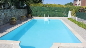 Una piscina rectangular con un muro de piedra en un lado y un seto verde en el otro.