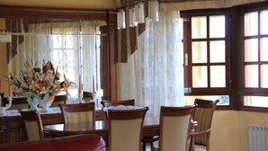 Un comedor con una mesa de madera, sillas, un jarrón de flores y una ventana con cortinas.