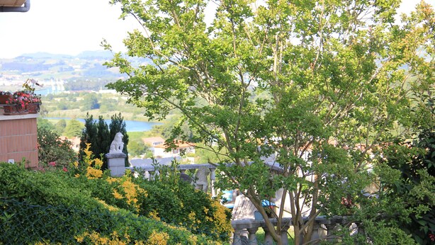 Un jardín ajardinado con una estatua, una valla y vistas a un lago y edificios a lo lejos.