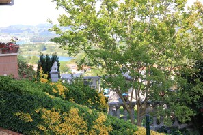 Ein angelegter Garten mit einer Statue, einem Zaun und Blick auf einen See sowie Gebäude in der Ferne.