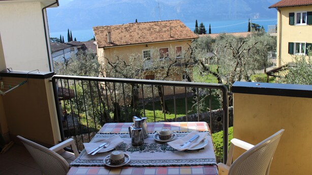 A balcony with a table set for two, overlooking a scenic view of mountains and a lake.