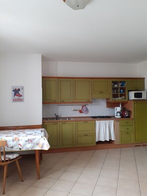 A kitchen with green cabinets, a microwave, and a table with a floral tablecloth.