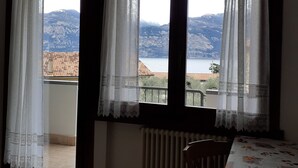 A room with a view of mountains and a lake. There is a table with a floral tablecloth and a chair.