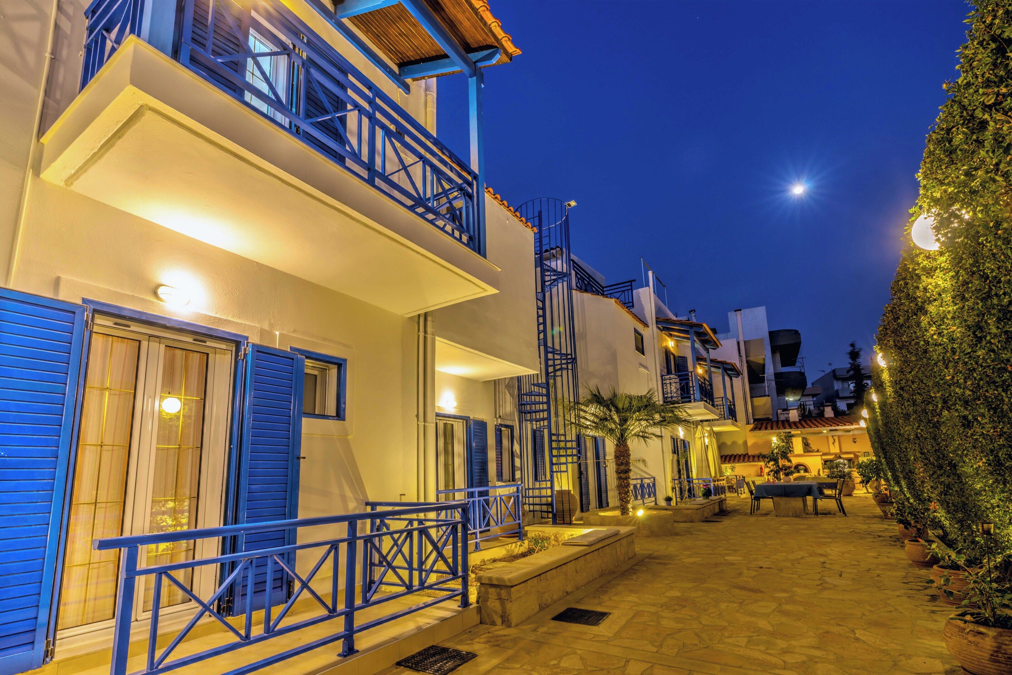 Un edificio con contraventanas azules, un balcón y un patio empedrado con mobiliario de exterior.