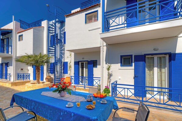 Une table dressée avec des aliments pour le petit-déjeuner, une nappe bleue et un balcon avec des balustrades bleues.