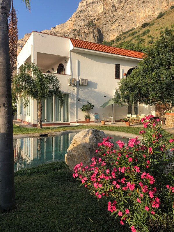 A modern building with a pool, surrounded by greenery and a mountain backdrop. - Villa between sea and mountain with private pool and sea view with private pool  (Capaci)