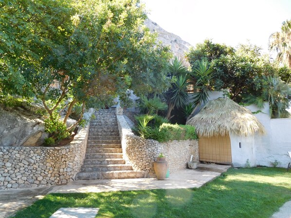 A stone staircase leading to a thatched-roof building, surrounded by lush greenery and a mountain backdrop. - Villa between sea and mountain with private pool and sea view with private pool  (Capaci)