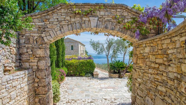 A stone archway leading to a courtyard with a stone building and a view of the sea. - Paleopetres Marnie - Private Pool - Sea Views - Beaches - North East Coast - (Nisaki)