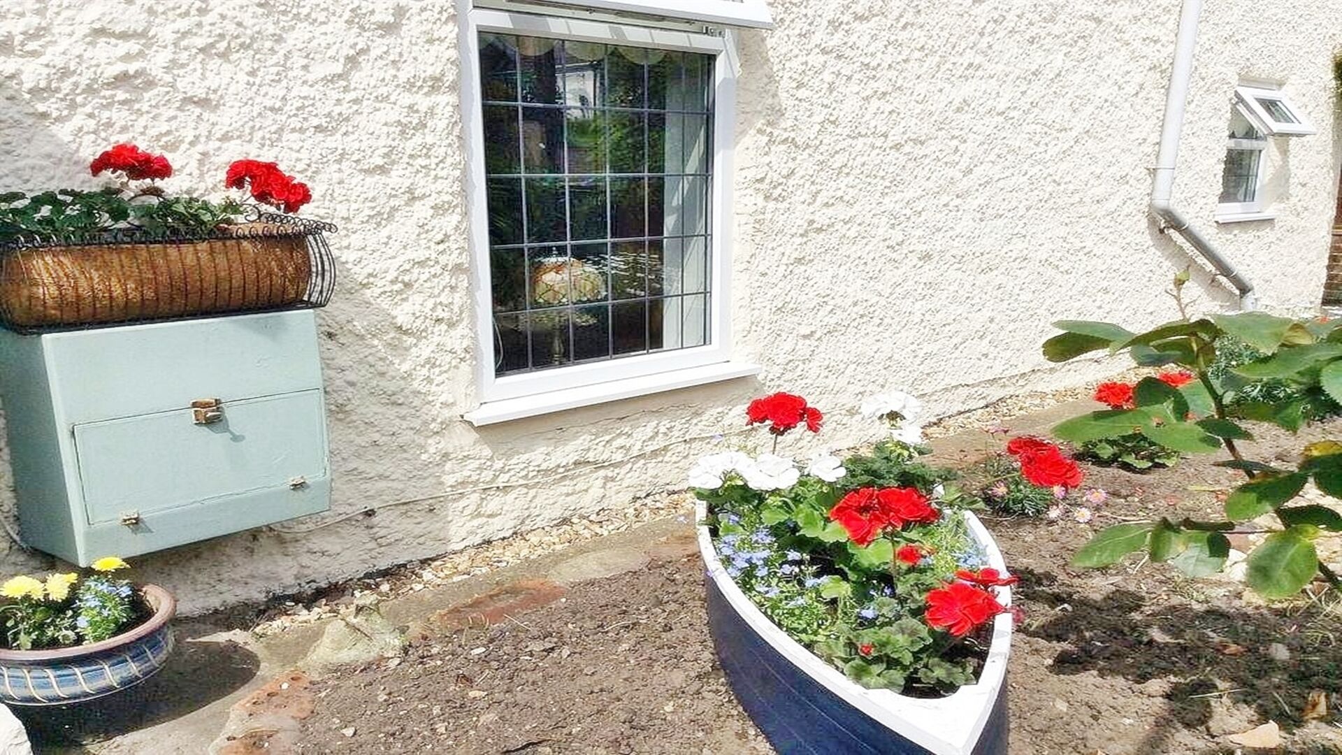 Un edificio rústico con una ventana, un mueble azul y macetas de flores.