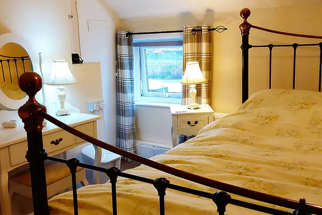 Un dormitorio con cama, mesitas de noche, un espejo y una ventana con cortinas.