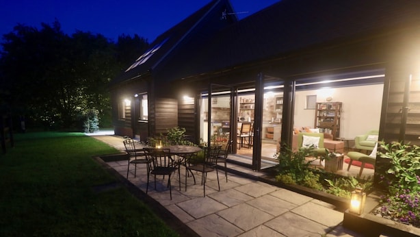 A house with a patio area featuring a table and chairs, surrounded by a garden with plants and a small tree. - High quality barn conversion near Cambridge to enjoy countryside & city (Cambridge)