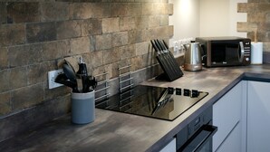 A modern kitchen with a built-in stove, microwave, and oven. There are wooden shelves above the counter and a basket on the lower shelf. - High quality barn conversion near Cambridge to enjoy countryside & city (Cambridge)