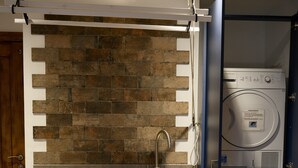 A compact kitchen with a built-in sink, a stone backsplash, and a stacked washer and dryer unit. - High quality barn conversion near Cambridge to enjoy countryside & city (Cambridge)