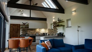 A modern loft-style living space with a dining area, kitchen, and a large blue sofa. - High quality barn conversion near Cambridge to enjoy countryside & city (Cambridge)