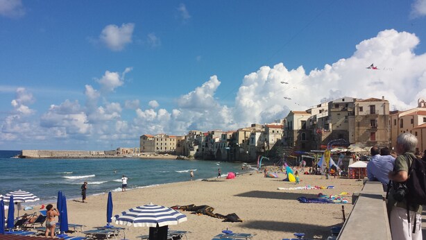 A beach with a stone wall, umbrellas, and beachgoers. - Archimedes Lounge in Cefalù (Cefalù)
