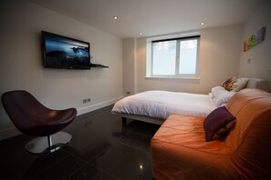A modern bedroom with a bed, a chair, and a TV on the wall.