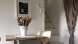 Un comedor con una mesa de madera, sillas blancas y un jarrón de flores secas.