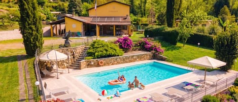 A swimming pool with lounge chairs and a covered seating area, surrounded by well-maintained gardens and a house named 'CASA ELIA'.
