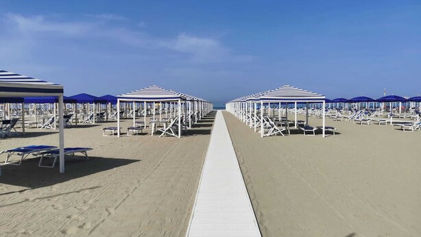 Une plage bordée de rangées de chaises longues et de parasols, une promenade blanche et un ciel dégagé.