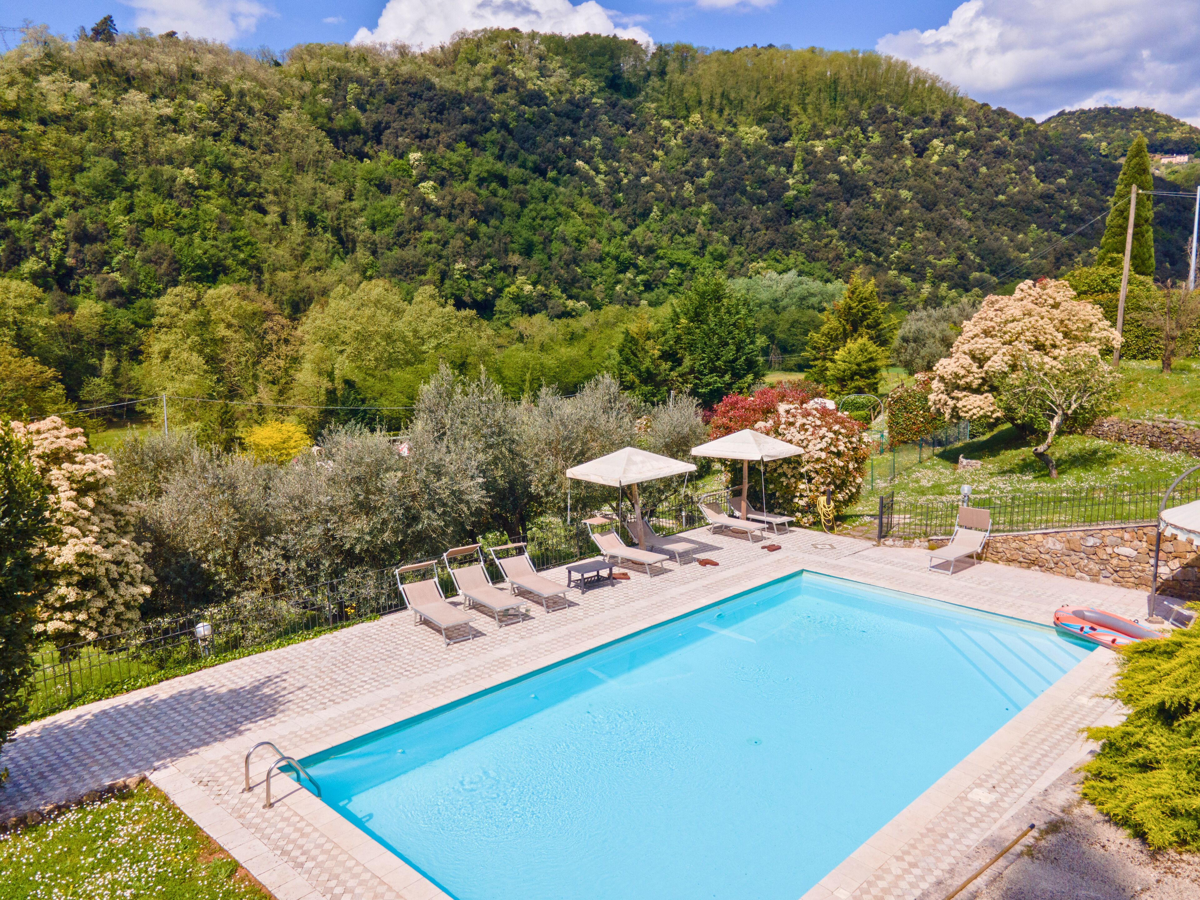 A swimming pool with lounge chairs and umbrellas, surrounded by lush greenery and hills.