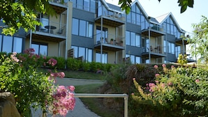 A multi-story residential building with balconies, a paved pathway, and surrounding greenery.