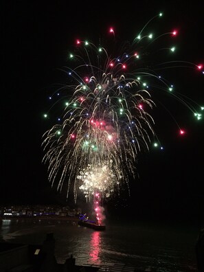 Espectáculo de fuegos artificiales nocturnos sobre una masa de agua, con un barco en primer plano.