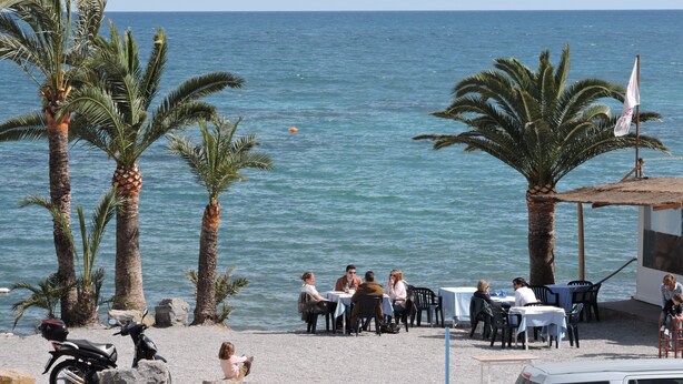 Un restaurant en bord de mer, doté d’une terrasse, de palmiers et offrant une vue sur l’océan.