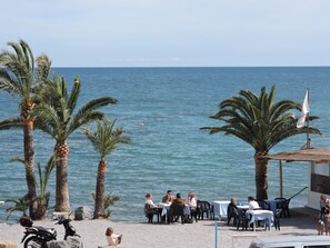 Un restaurante frente al mar con terraza, palmeras y vistas al océano.