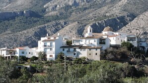 Un village côtier aux bâtiments blancs, une église dotée d’un clocher et un paysage montagneux en arrière-plan.